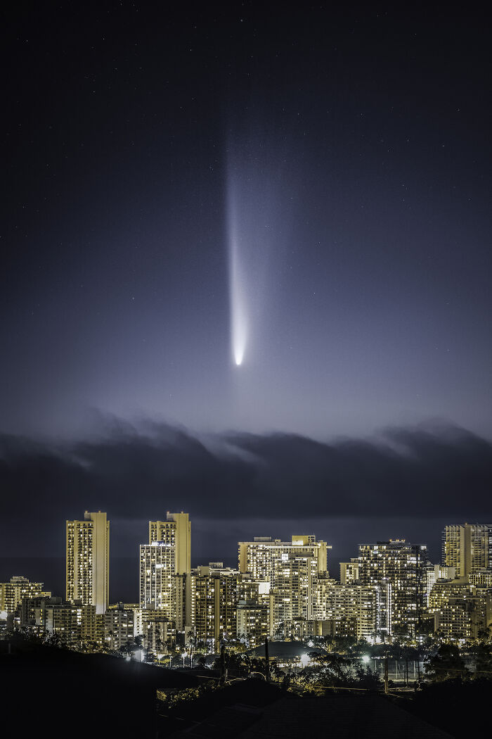 City skyline at night with a bright comet streaking across the sky, featured in breathtaking space photos shortlist.