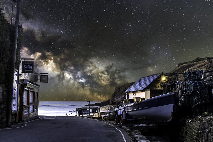 Night sky full of stars and the Milky Way over a coastal village with boats, showcasing breathtaking space photography.