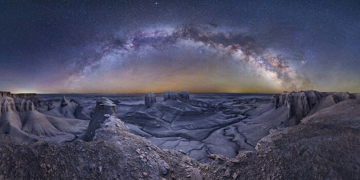 Panoramic night sky with the Milky Way arching over a rugged desert landscape in breathtaking space photography.