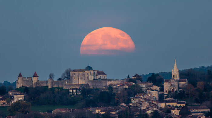A large orange moon rising behind a historic village, showcasing breathtaking space photography from the 2025 shortlist.