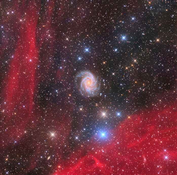 Spiral galaxy surrounded by stars and red nebulae showcasing breathtaking space photos from astronomy photography.