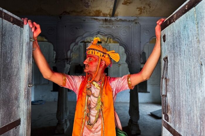 Man in traditional attire with vibrant colors standing in an old building, a powerful street photo capturing the soul of India.