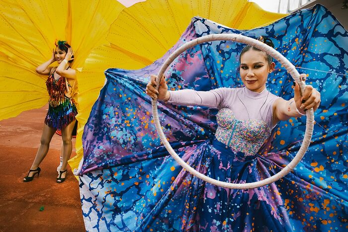 Two women dressed in vibrant colorful costumes with large flowing fabric, captured in a powerful street photo from India.