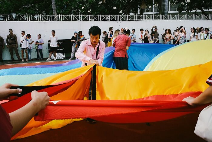 People unfolding a large colorful fabric in a vibrant street scene, showcasing powerful street photos of India.