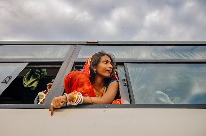 Two Indian women in traditional attire leaning out of a bus window, capturing powerful street photo moments in India.