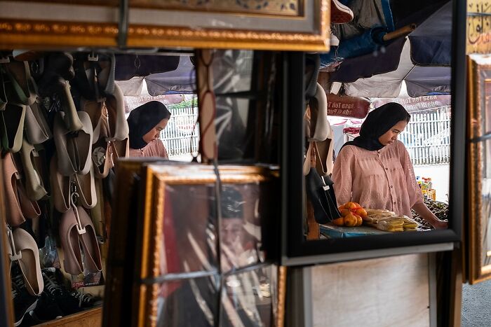 Woman in a street market reflected in framed photos and shoes, capturing the soul of India in a powerful street photo.