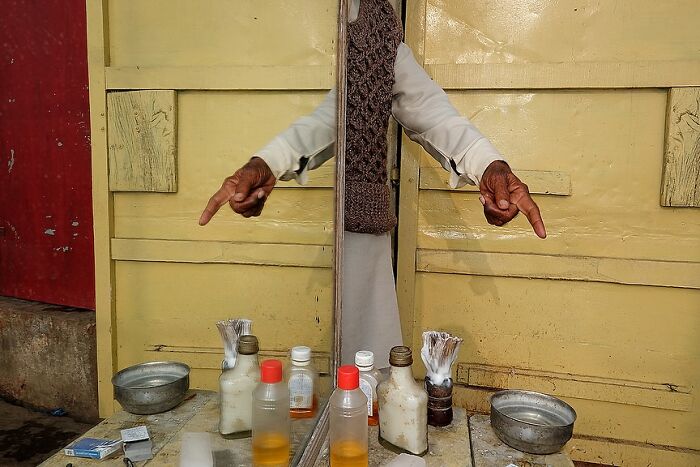 Man pointing down with both hands reflected in a mirror among grooming items in a powerful street photo capturing the soul of India.