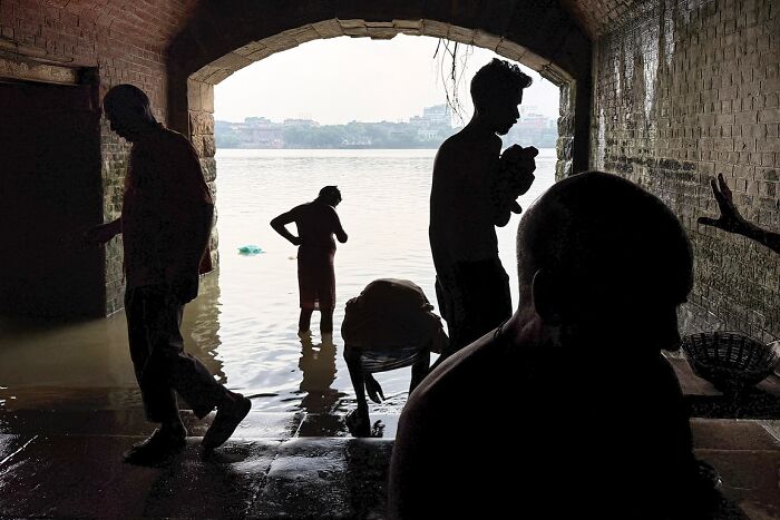 Silhouetted figures near water under an archway in a powerful street photo capturing the soul of India by Rohit Vohra.