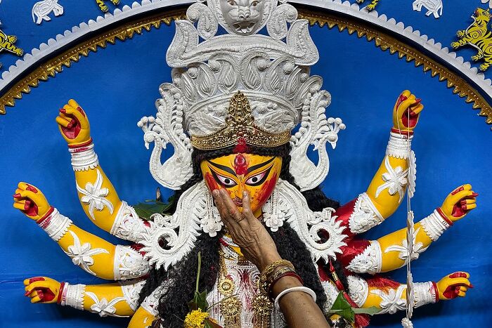 Hand painting a vibrant Durga idol during a traditional Indian festival, capturing powerful street photography in India.