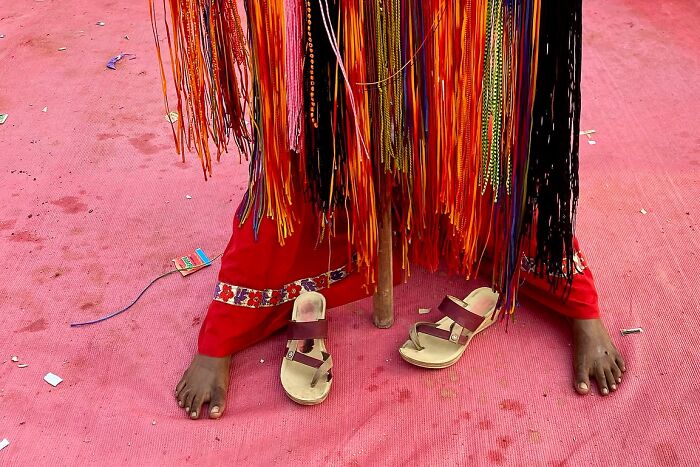 Bare feet and sandals on a red mat with colorful hanging threads in a powerful street photo capturing the soul of India.