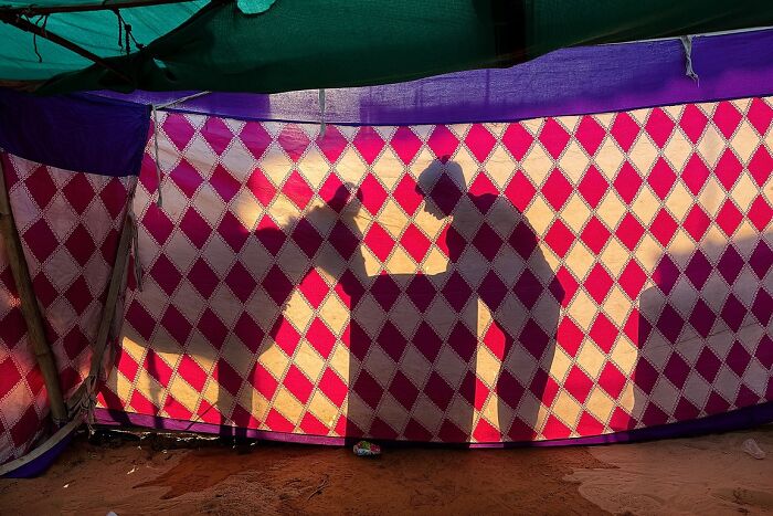 Shadows of two people interacting against a patterned cloth backdrop in a powerful street photo capturing the soul of India.