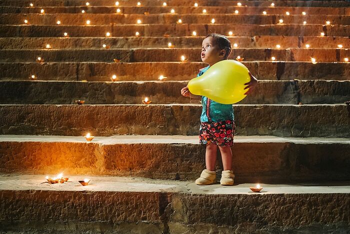 Young child holding a yellow balloon among oil lamps on stone steps in powerful street photos capturing the soul of India.