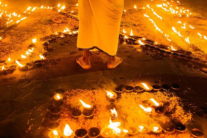 Feet of a person standing barefoot amidst traditional oil lamps during a vibrant street festival in India, street photos.