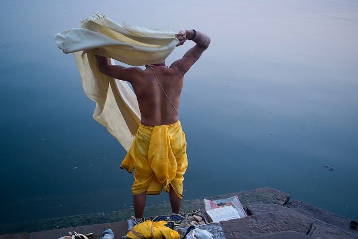 Man in traditional attire drying cloth by riverbank in a powerful street photo capturing the soul of India.