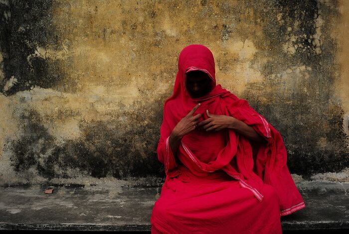 Woman in vibrant red traditional attire sitting against a textured wall in powerful street photos capturing the soul of India.