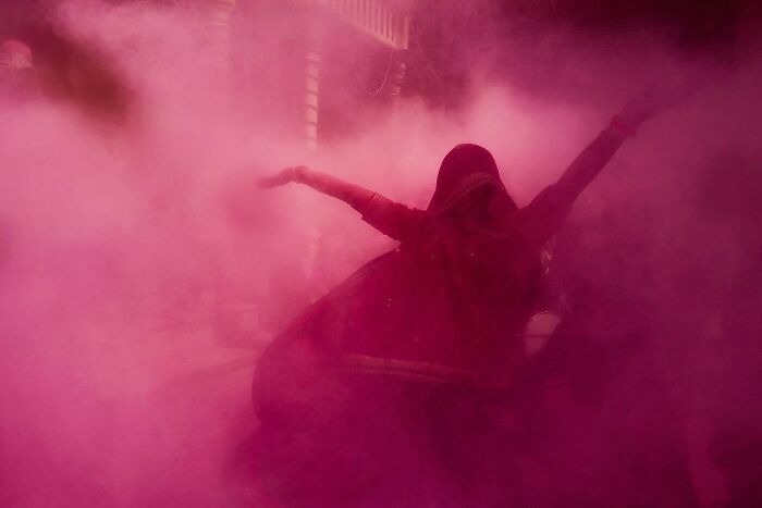 Woman dancing joyfully in a vibrant cloud of pink powder during a street celebration in India street photos.