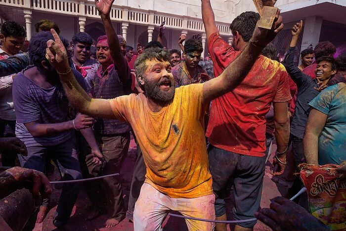 Man covered in vibrant colors dancing joyfully during a street festival in India in powerful street photos capturing the soul.