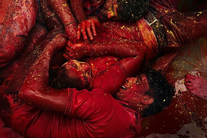 Men covered in red paint embracing each other during a vibrant street festival in India, capturing powerful street moments.