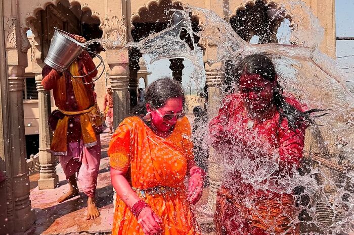 Two women in colorful traditional attire splashed with water during vibrant street celebration in India, captured by Rohit Vohra.