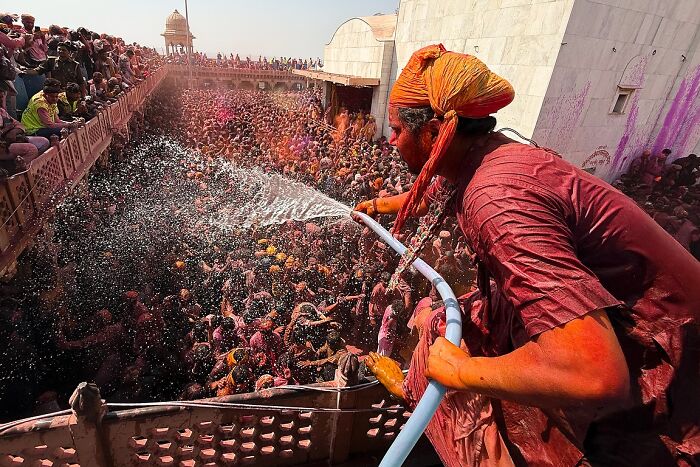 Man drenched in color sprays water over a vibrant crowd during a street festival in India capturing powerful street photos.