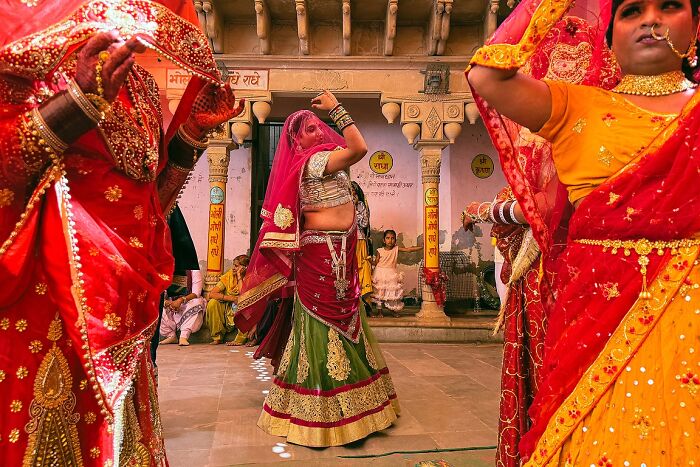Women in vibrant traditional Indian attire dancing during a street celebration in India, captured in a powerful street photo.
