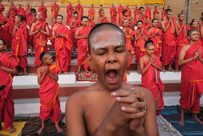 Young boy with eyes closed and hands clasped in prayer among monks dressed in orange robes in a powerful street photo of India.