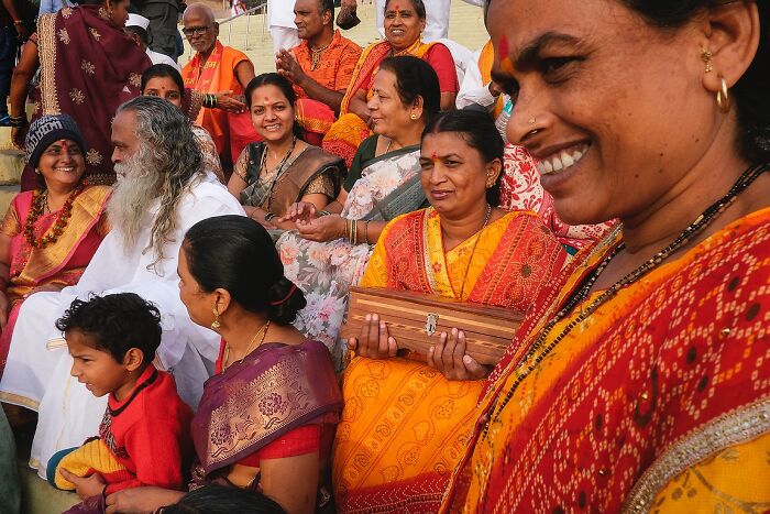 Group of Indian people in colorful traditional attire smiling and sitting outdoors in a vibrant street photo capturing the soul of India.