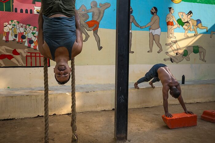 Man hanging upside down on rope and another doing yoga in an Indian street gym, a powerful street photo capturing India's soul.