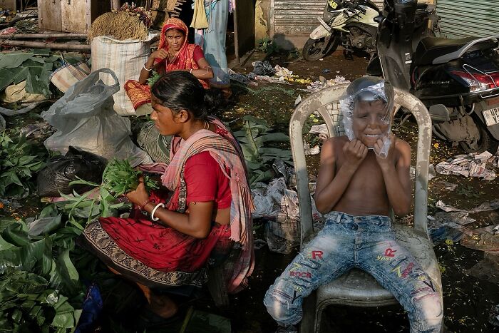 Street photo showing Indian woman sorting greens and a child playing with a plastic bag, capturing the soul of India.