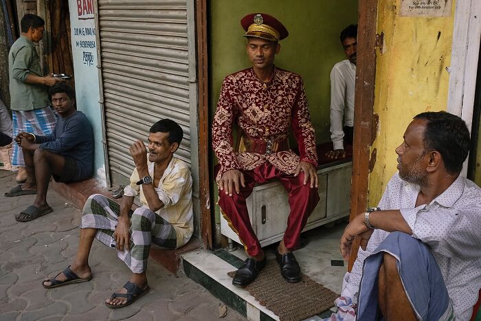 Street photo capturing men in traditional and casual attire sitting outside shops in India’s vibrant street life.