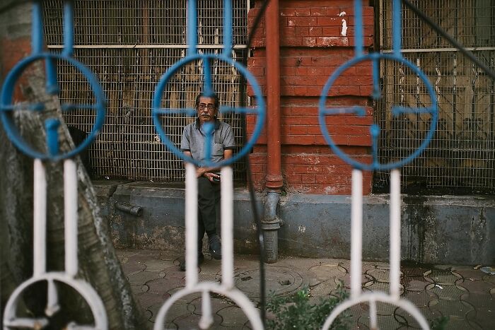 Street photo of an elderly man sitting by a red brick wall, capturing the soul of India through powerful street photography.