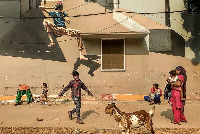Street photo capturing daily life in India with locals and a mural, showcasing powerful street photography by Rohit Vohra.