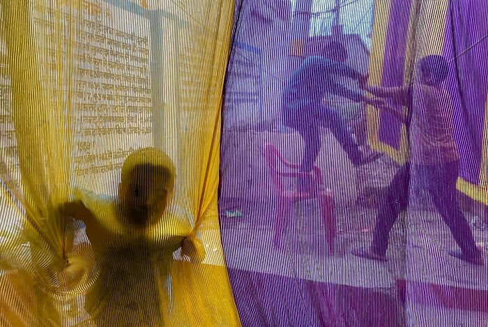 Child playing behind yellow and purple fabric, with people walking outside, powerful street photos capturing the soul of India.