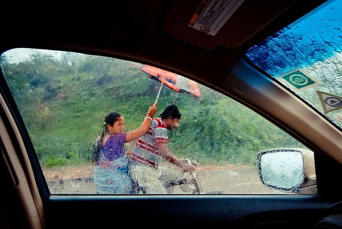 Street photo showing two people on a bike in the rain, capturing the soul of India with an umbrella.