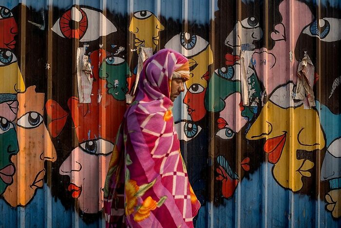 Man wrapped in a colorful shawl walking past vibrant street photos capturing the soul of India on a mural background.