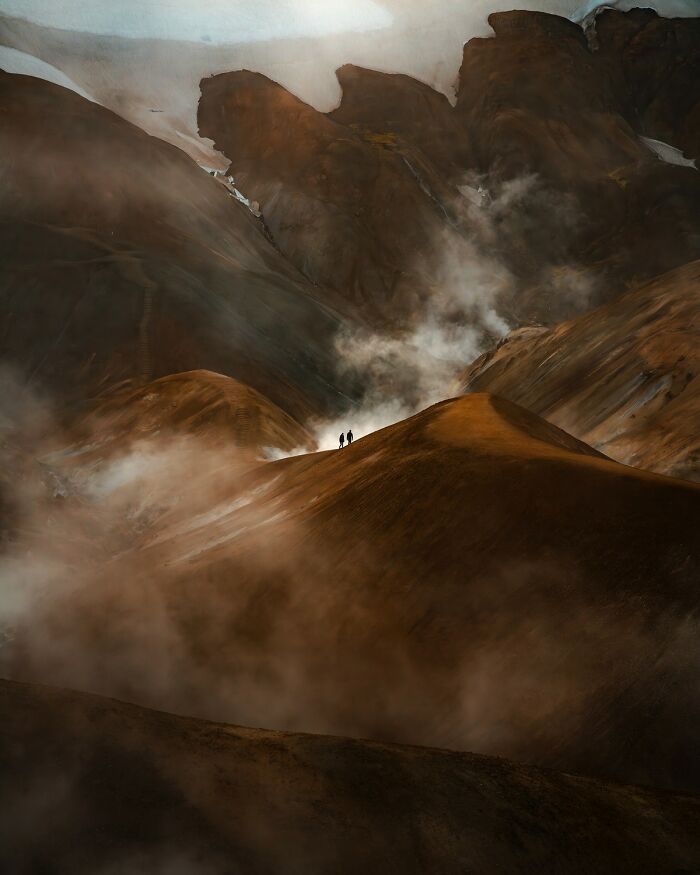 Two hikers stand on a misty hill amid rugged mountains in a breathtaking color photography landscape.