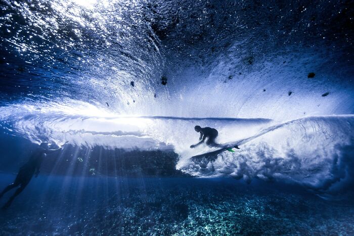 Underwater color photography of a surfer riding a wave, showcasing vibrant blue hues and dynamic motion from the Refocus Awards.