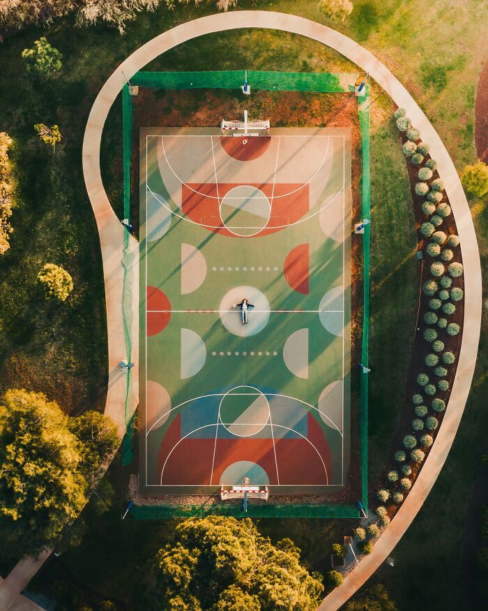 Aerial view of a colorful basketball court surrounded by greenery, showcasing vibrant color photography.