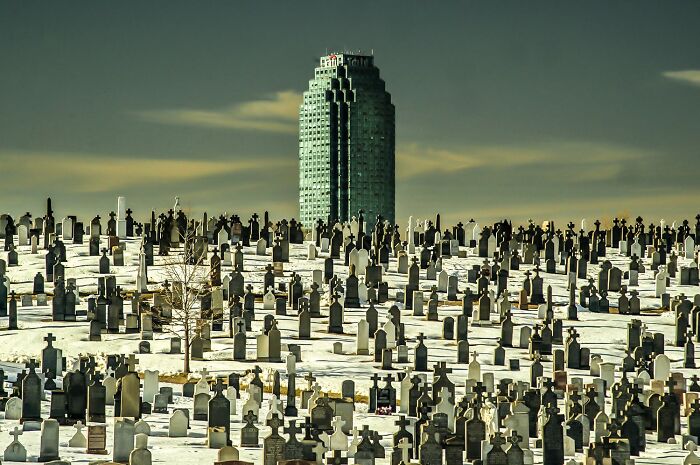 A vast cemetery covered in snow with numerous tombstones and a tall building in the background, showcasing color photography.
