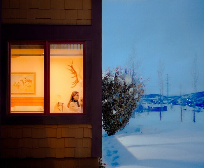 Warm interior glow with a woman inside contrasts with a snowy blue exterior landscape in stunning color photography.