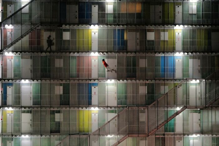 Night view of a colorful building facade with multiple doors and two people walking, showcasing stunning color photography.