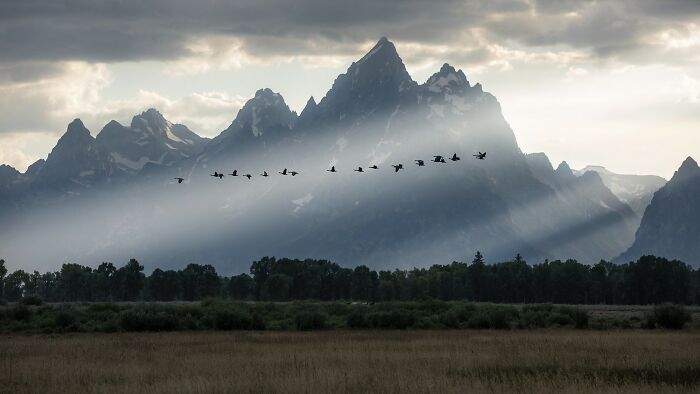 Mountain range with sun rays breaking through clouds, highlighting birds in flight in breathtaking color photography.