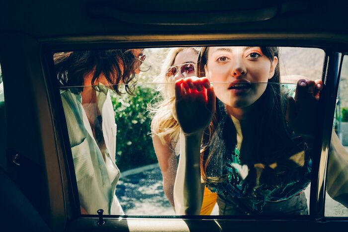Three women captured in vivid color photography, looking through a car window revealing candid emotions and natural light.