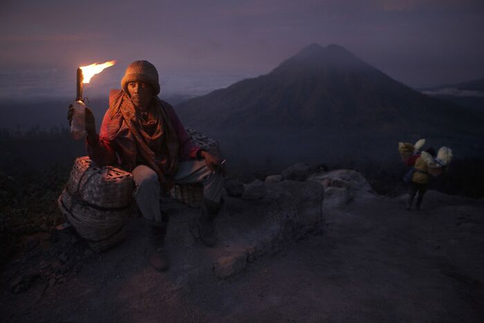 Man holding a torch at dusk on a mountain path, showcasing breathtaking color photography from the Refocus Awards.