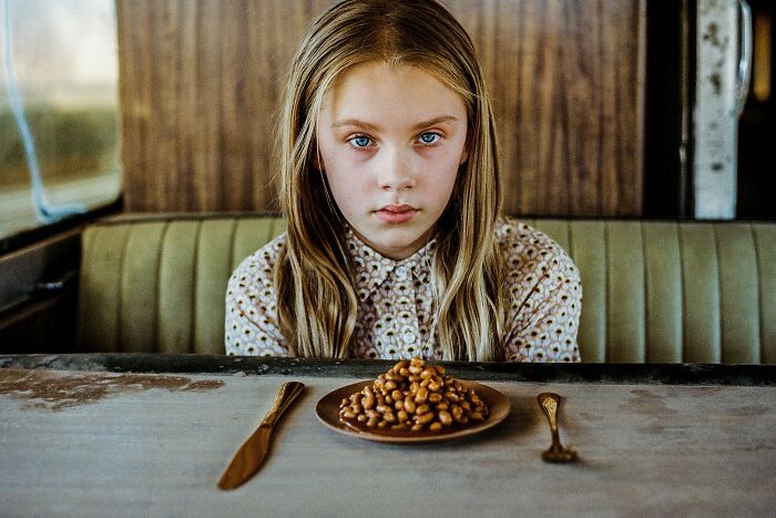 Young girl with blue eyes sitting at a table with beans, showcasing impactful color photography in a vintage setting.