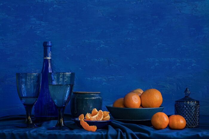 Still life with blue glassware and vibrant orange fruits, showcasing stunning color photography from the 2025 Refocus Awards.