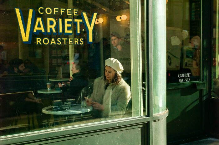 Woman in a white beret sitting inside a coffee shop, captured in vibrant color photography with natural light reflections.