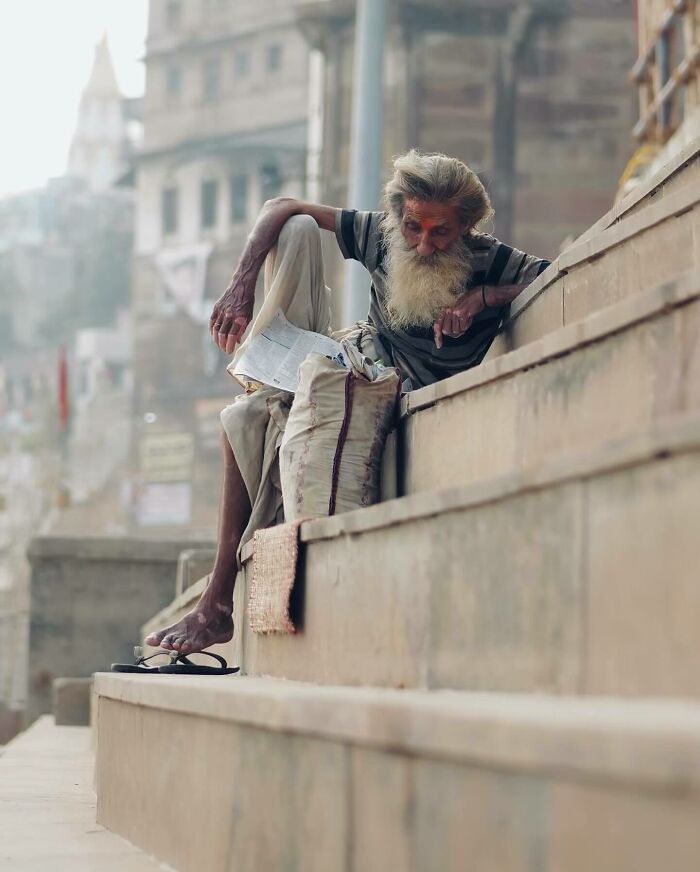 Elderly man with a long beard sitting on stone steps, reading a paper, captured in a stunning Asia photography moment.