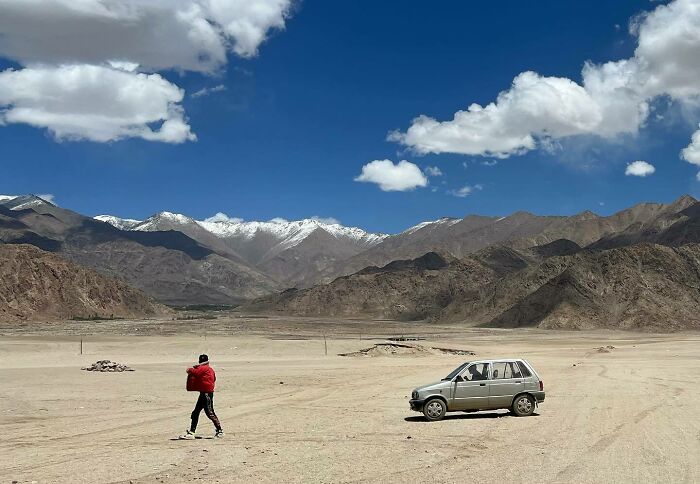 Person walking near a car in a vast desert landscape with mountains under a blue sky, inspiring to explore Asia photography.