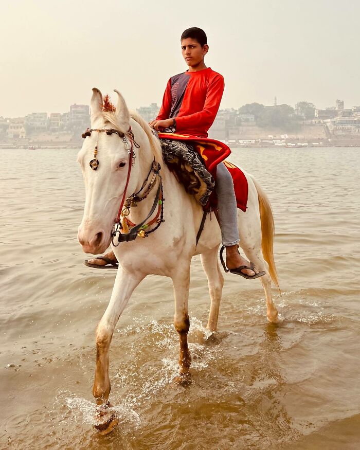 Boy wearing red riding a white horse through shallow water, capturing the spirit of exploring Asia in a stunning photography scene.